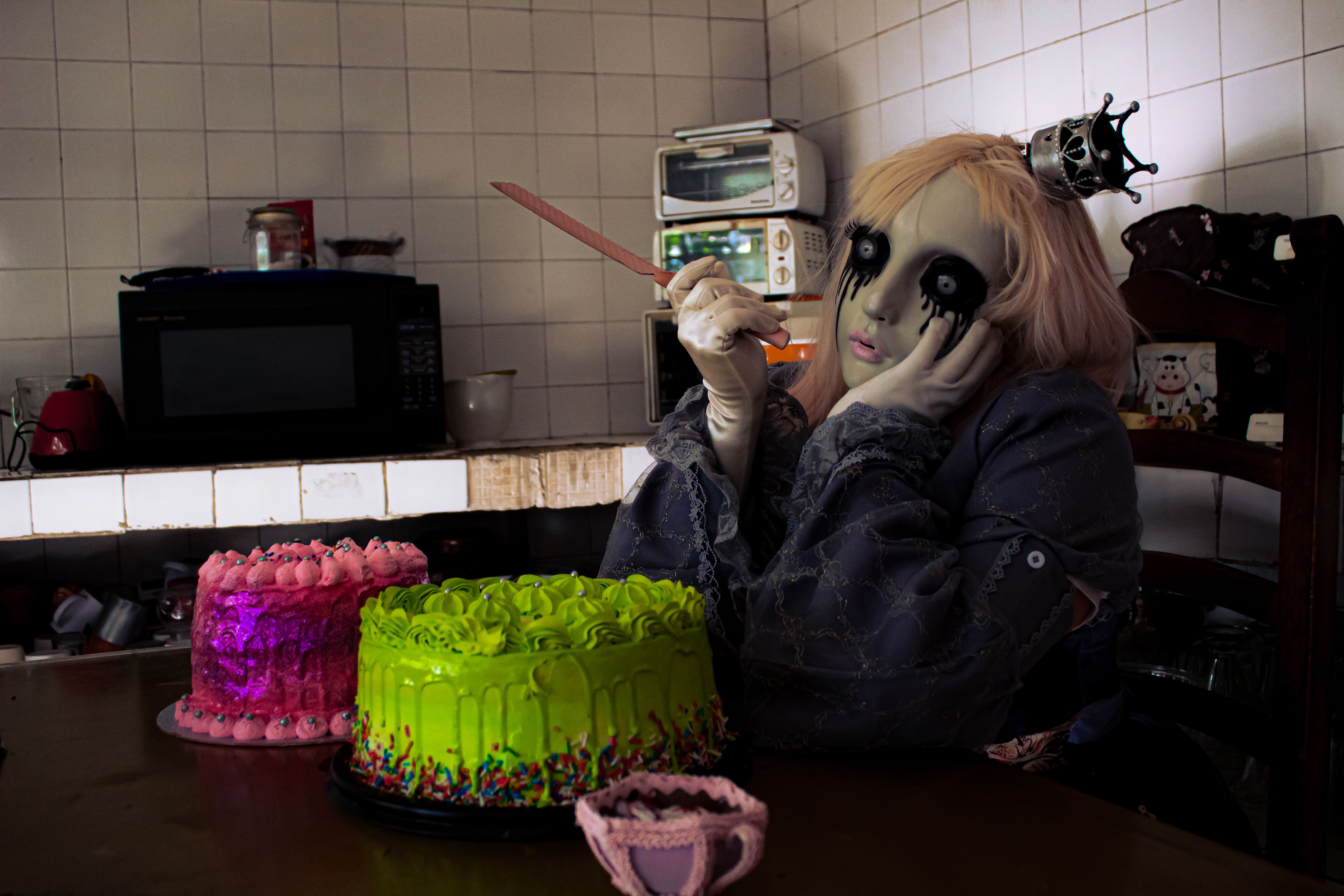 A person in gothic makeup and attire sitting at a table with colorful cakes in Ciudad de México.