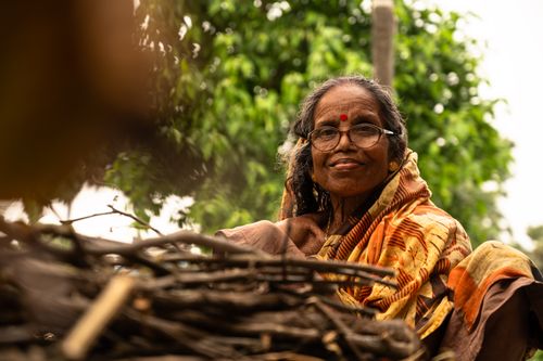 Free Elderly woman in sari smiling near stacked firewood, outdoors. Stock Photo