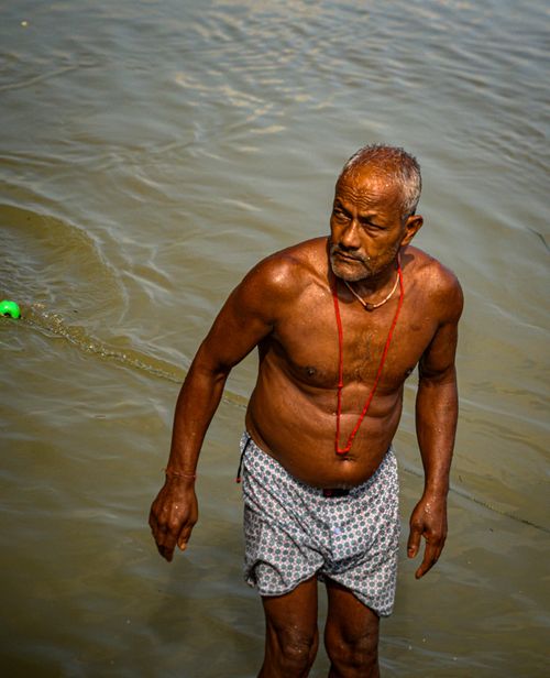 Free Senior adult man wading in calm river waters, wearing patterned shorts. Serene outdoor setting. Stock Photo