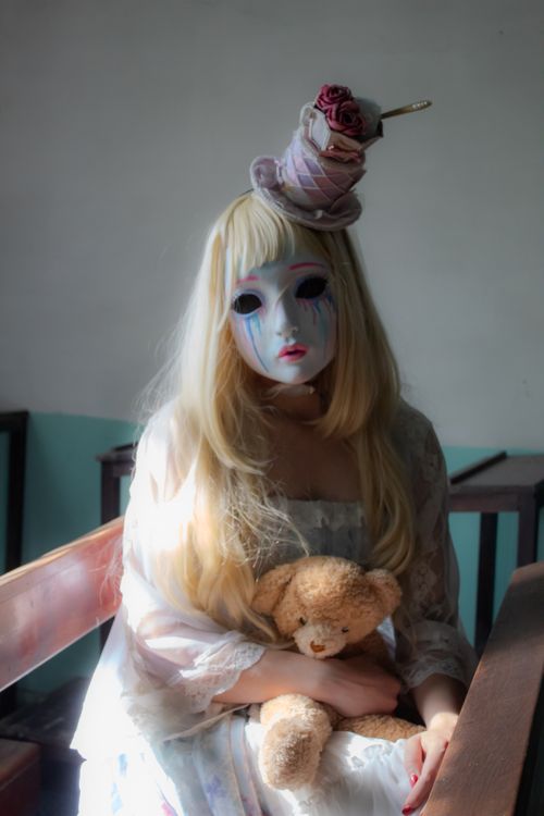 Free Surreal portrait of a woman in a mask holding a teddy bear, evoking mystery and intrigue. Stock Photo
