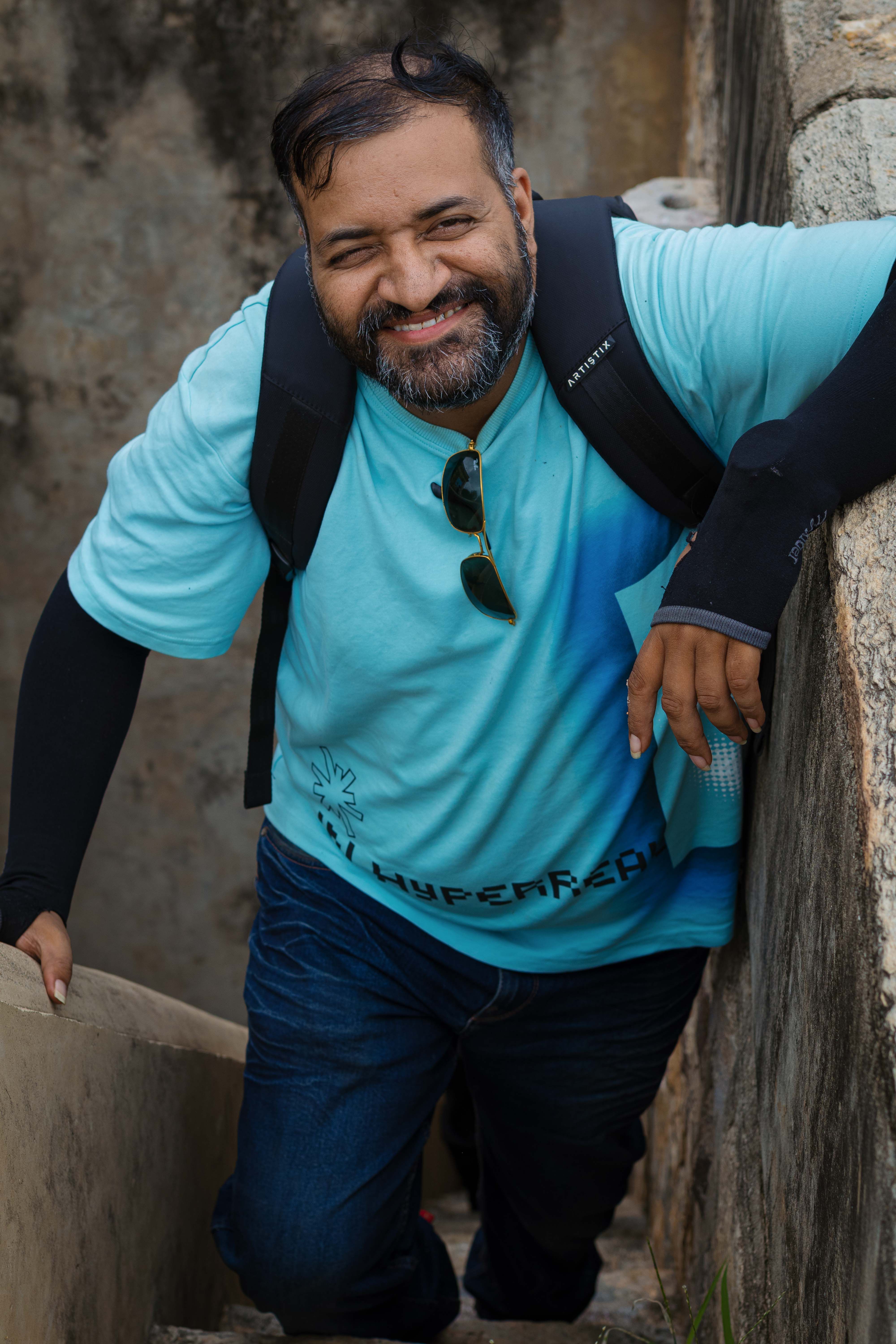 Man with backpack and sunglasses climbing stairs with a smile, Jaipur.