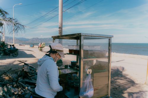 Free A street vendor selling food in a mobile cart by a sunny beach, with a scenic ocean view. Stock Photo