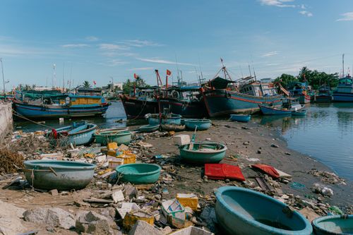 Free Colorful fishing boats docked at a polluted harbor with scattered debris under a clear blue sky. Stock Photo