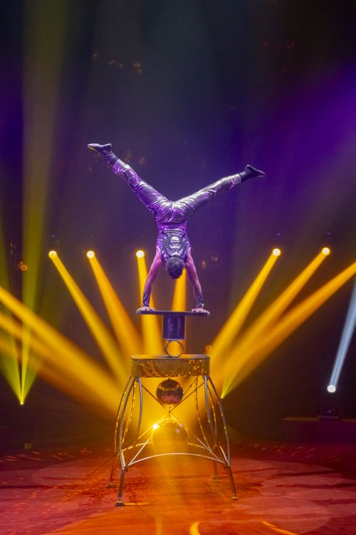 Free Daring acrobat performs handstand on stacked chairs with vibrant stage lighting. Stock Photo
