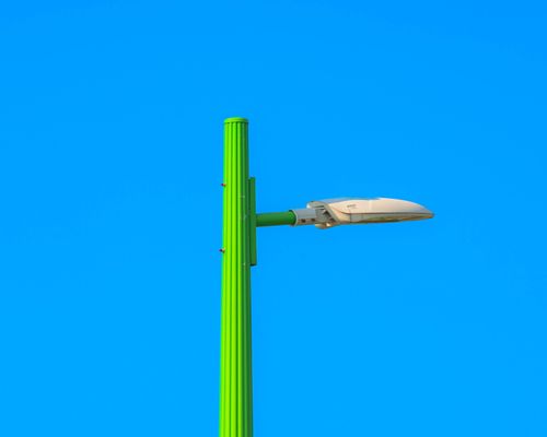 Free Bright green street lamp contrasting with a clear blue sky, capturing modern urban design. Stock Photo