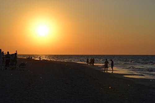 Várias Pessoas Em Pé Na Praia Durante O Pôr Do Sol