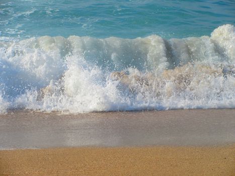 Waves crashing onto a sandy beach under sunlight create a scenic coastal view.