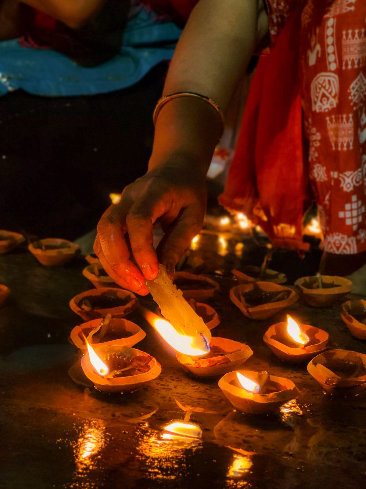 A woman lighting rows of small clay oil lamps set out on the ground at a festival of lights in India