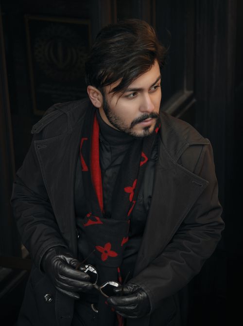 Free A trendy man in a black coat and gloves with a red-accented scarf, posing indoors. Stock Photo