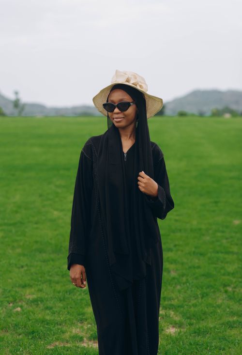 Free A fashionable woman wearing sunglasses and a hijab enjoys a sunny day in a lush green park. Stock Photo