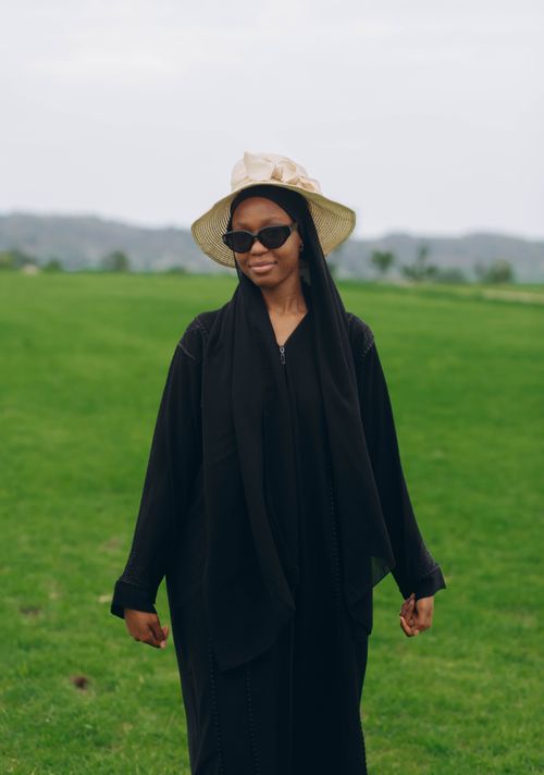 Free Stylish woman in sunglasses and hat walking in a green field, exuding elegance and charm. Stock Photo