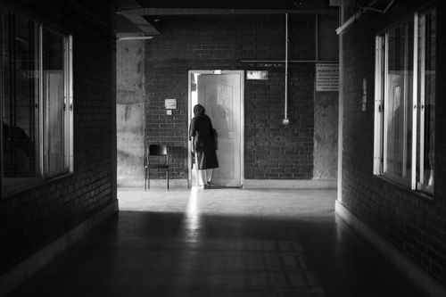Free A solitary person standing in a dimly lit corridor with a door slightly open, captured in monochrome. Stock Photo