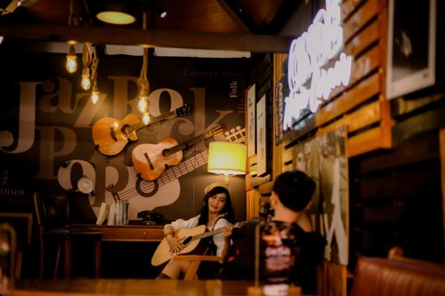 Free A woman plays guitar in a warmly lit cafe, surrounded by musical decor. Stock Photo