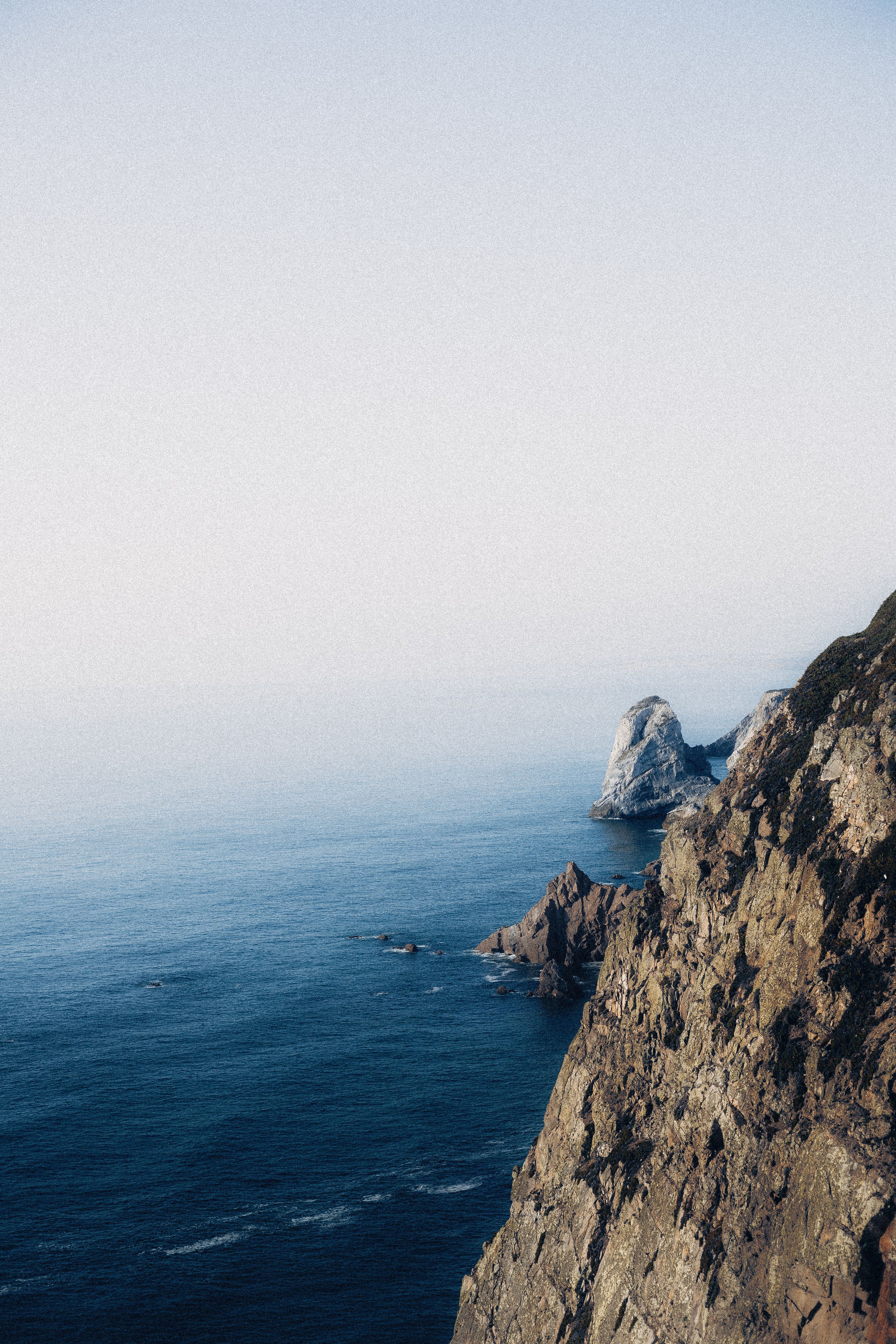 Stunning view of rugged coastal cliffs meeting the vast ocean under a clear sky.