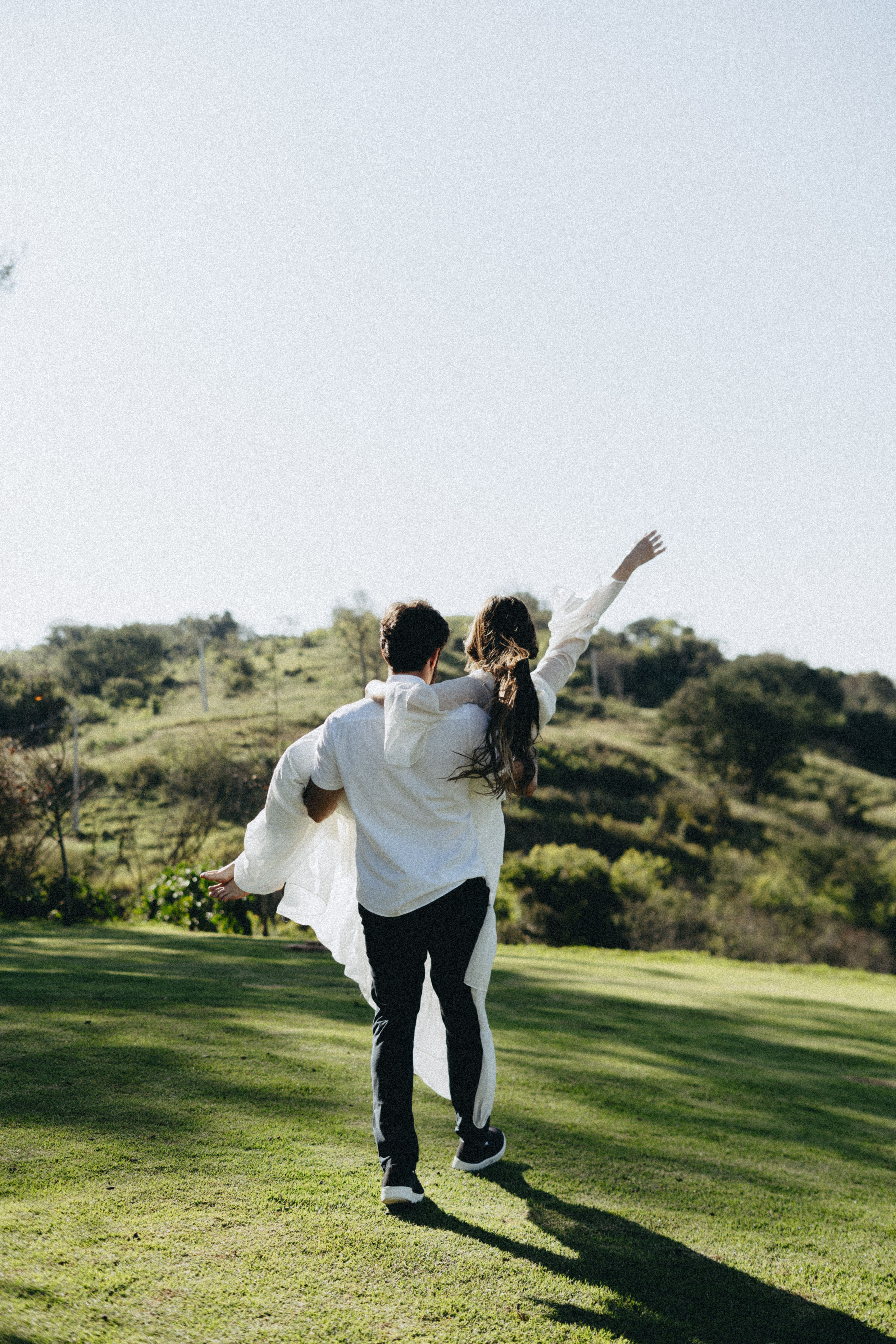 A couple enjoying a playful moment in a sunny outdoor landscape.