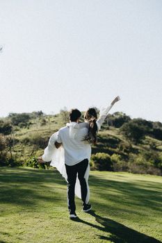 A couple enjoying a playful moment in a sunny outdoor landscape.