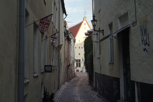 Picturesque narrow alleyway with medieval architecture and flags in a European city at sunset.