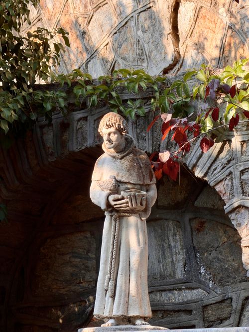 Free Serene stone statue of a monk within a historic stone arch, surrounded by fresh leaves. Stock Photo