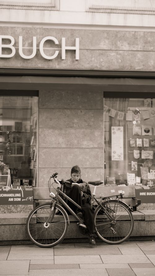 Free A person reading outside a bookstore with a bicycle in a sepia-toned street scene. Stock Photo