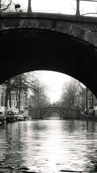 A monochrome capture of Amsterdam's iconic canals, featuring multiple bridges and serene reflections.