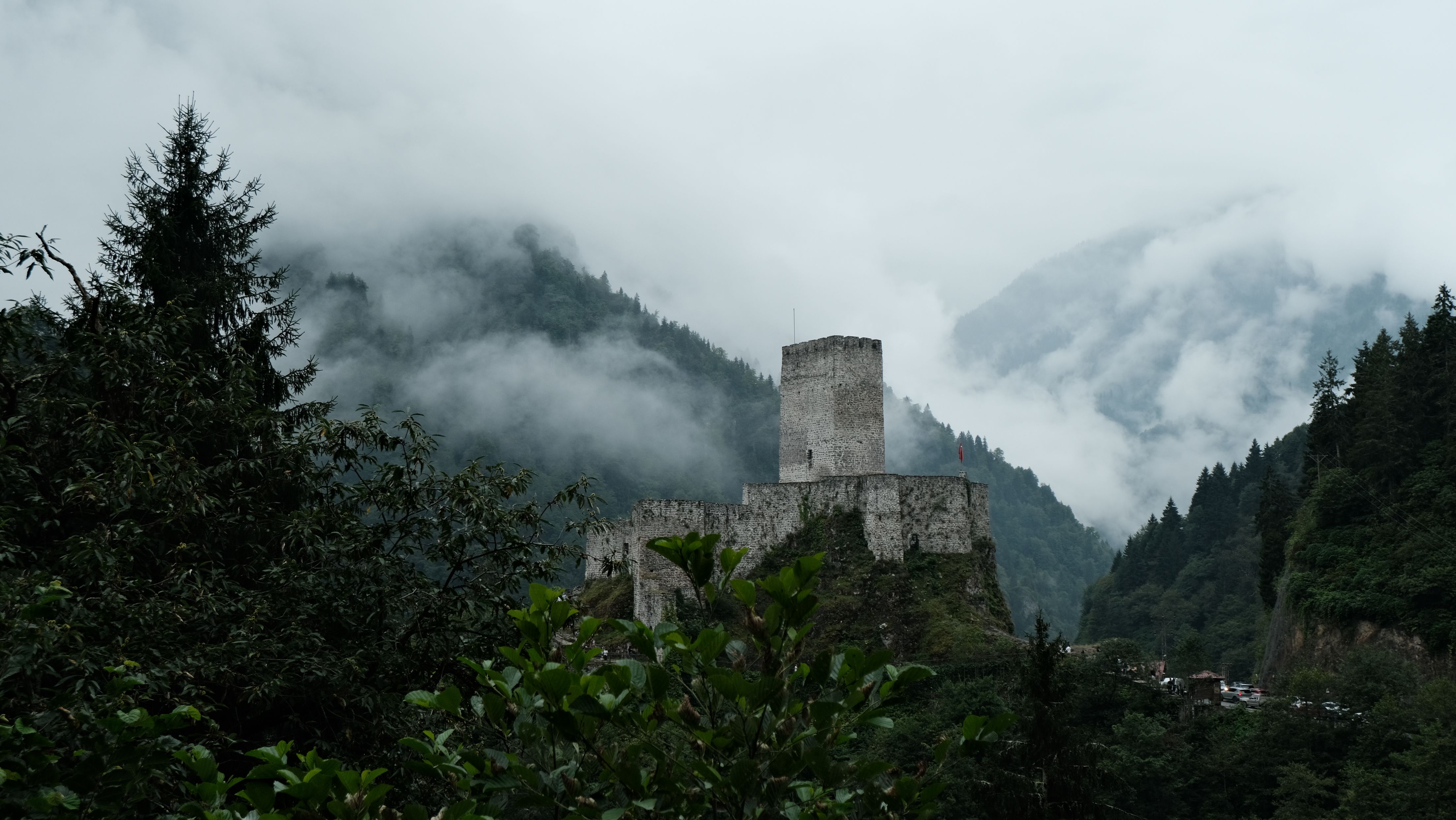 A mystical medieval castle surrounded by misty mountains and lush greenery.
