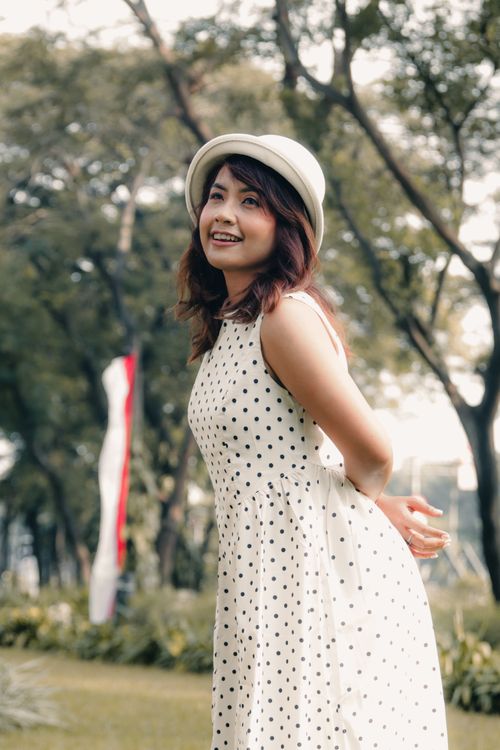 Free Smiling woman in white dress and hat enjoying a sunny day in a Jakarta park. Stock Photo
