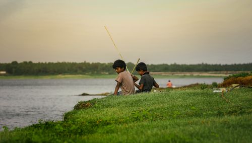 Free Two boys enjoy a relaxing fishing experience by a serene riverside during the evening. Stock Photo