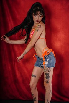 Model posing in vibrant attire and showcasing tattoos against a striking red backdrop.