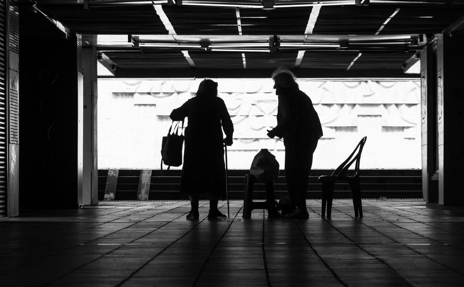 Silueta en blanco y negro de dos ancianos en una zona urbana, que evoca una sensación de misterio e intimidad.