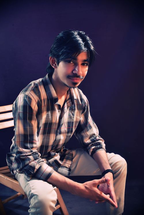 Free A young man in a plaid shirt seated indoors against a dark background. Stock Photo