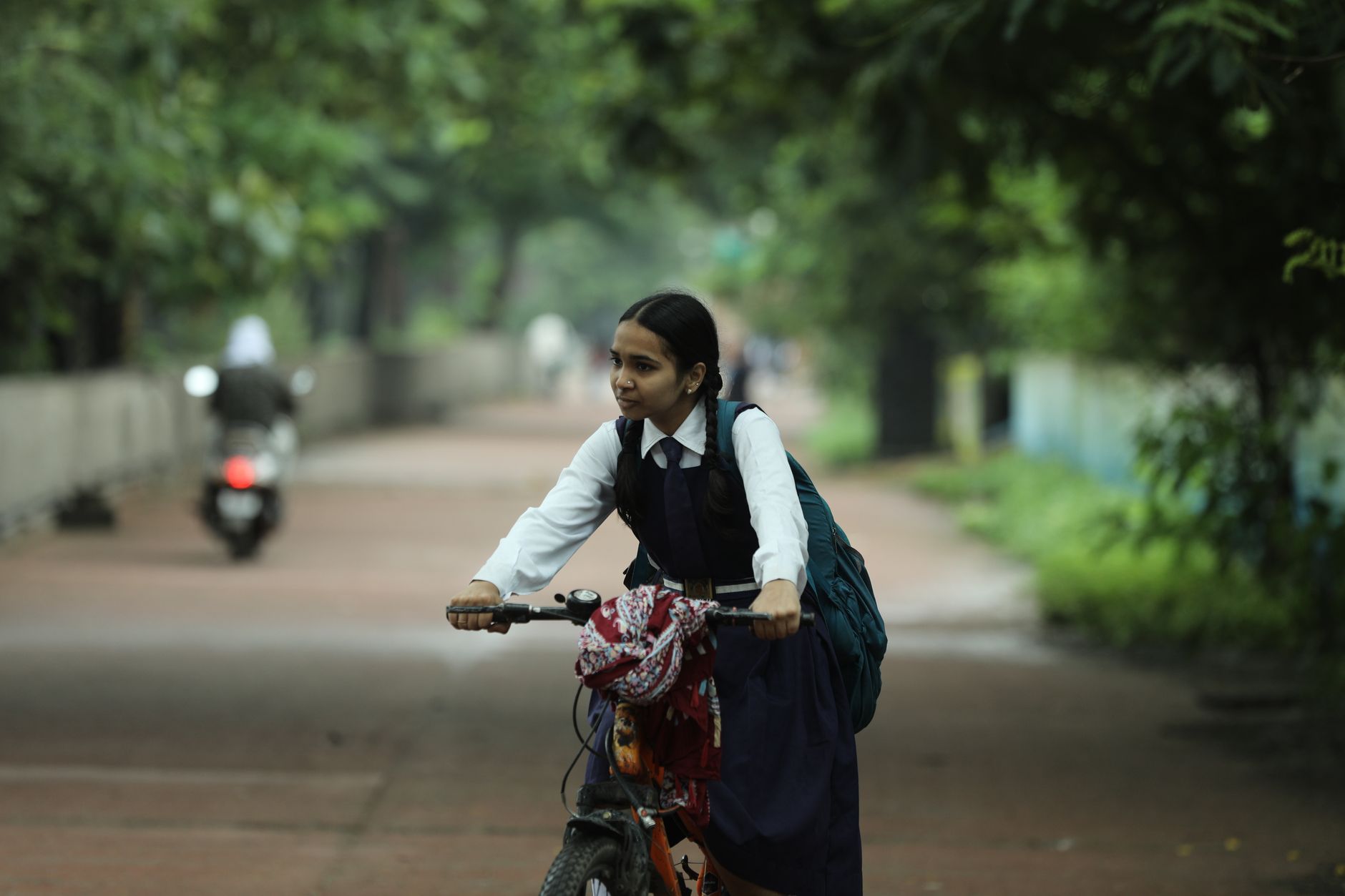 A young Indian girl rides a bicycle through a lush, green pathway in Raipur, capturing the serene daily commute.