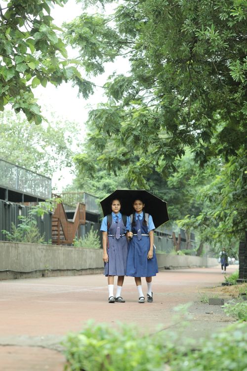 Free Two schoolgirls in uniform standing under an umbrella on a tree-lined street in Raipur, India. Stock Photo