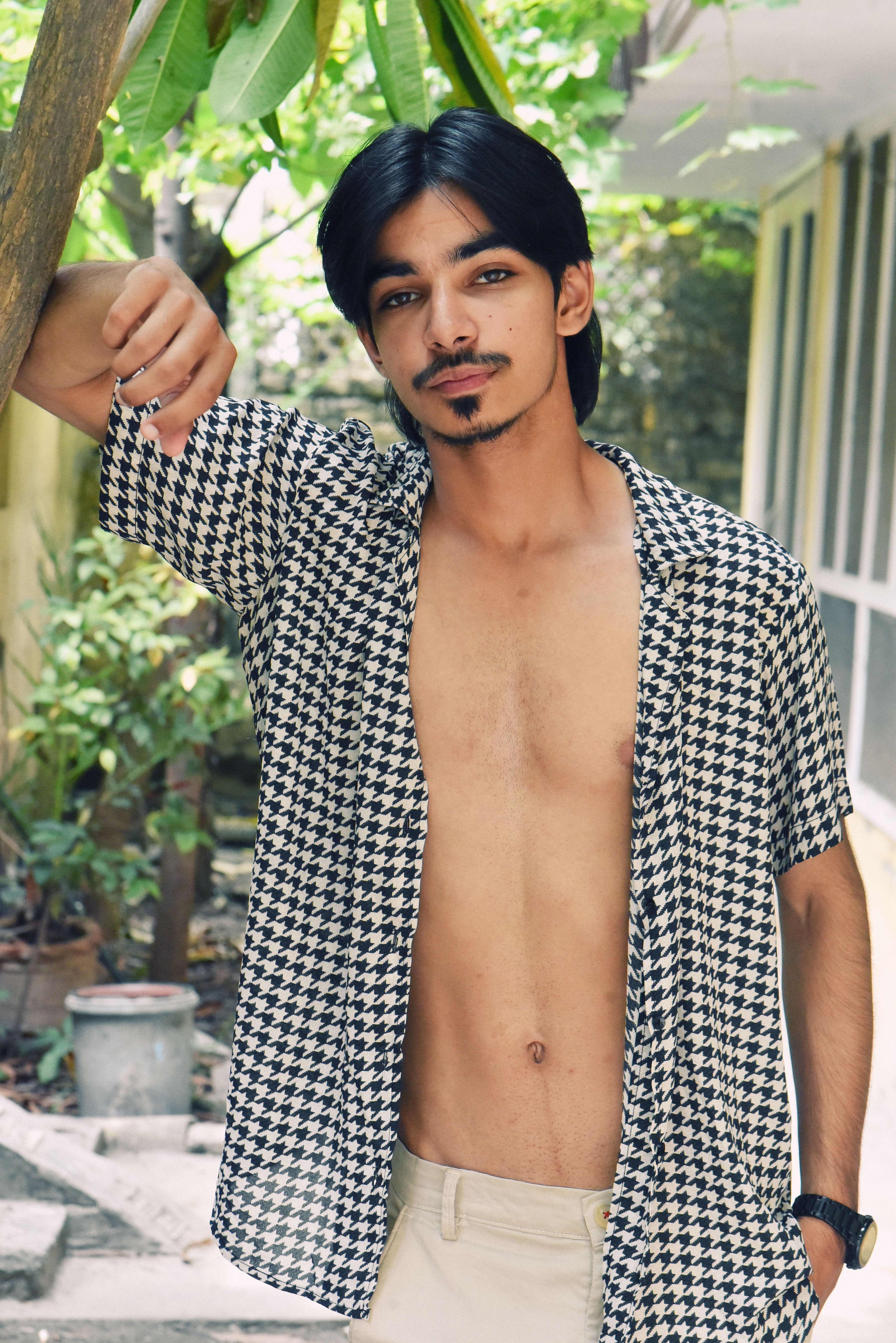 Casual portrait of a young man in a patterned shirt posing outdoors in summer.