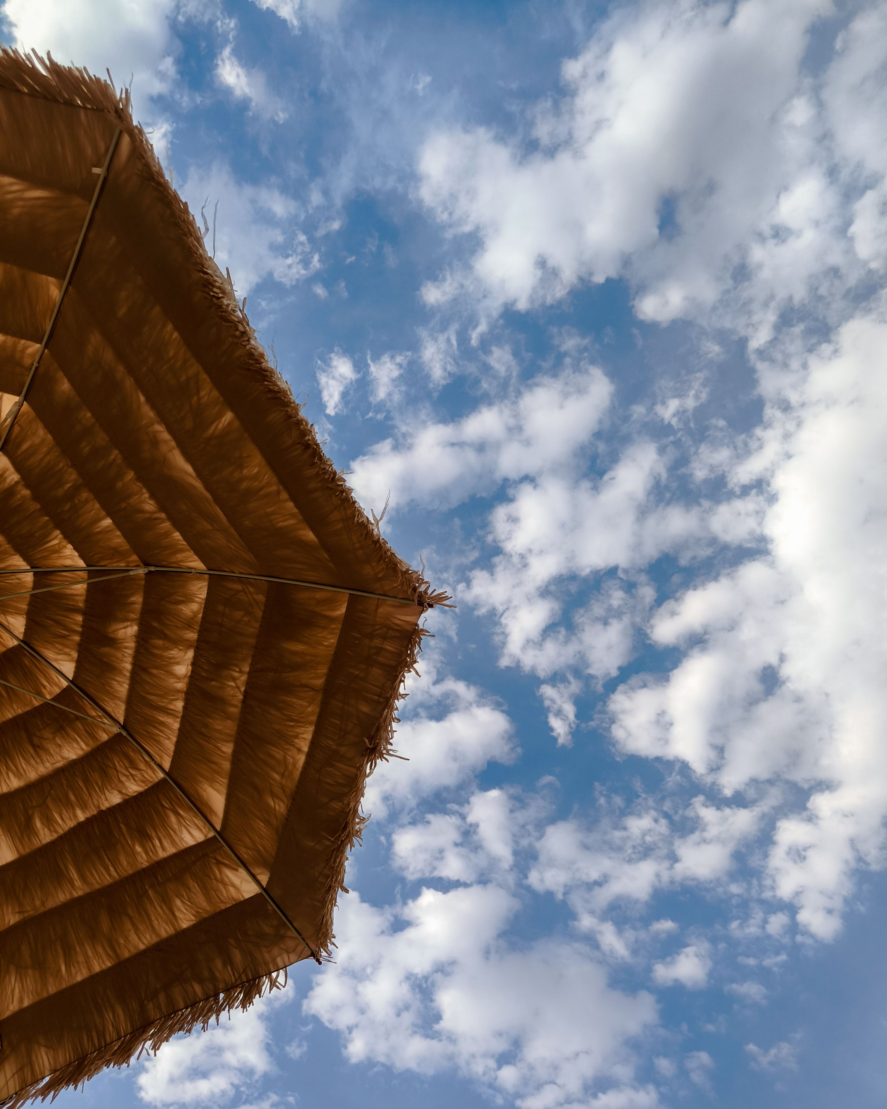 Straw beach umbrella seen from below against a partly cloudy sky, perfect for summer relaxation themes.