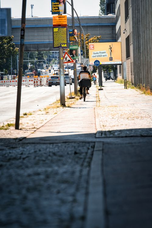 Free A cyclist rides down a sunlit street in Berlin, Germany, with urban buildings and traffic. Stock Photo