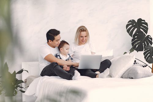 Man and Woman Sitting on White Bed Using Laptop Computer