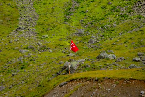 Free Turkish flag waving on a rocky hillside in Rize, Türkiye, showcasing natural landscape and national pride. Stock Photo
