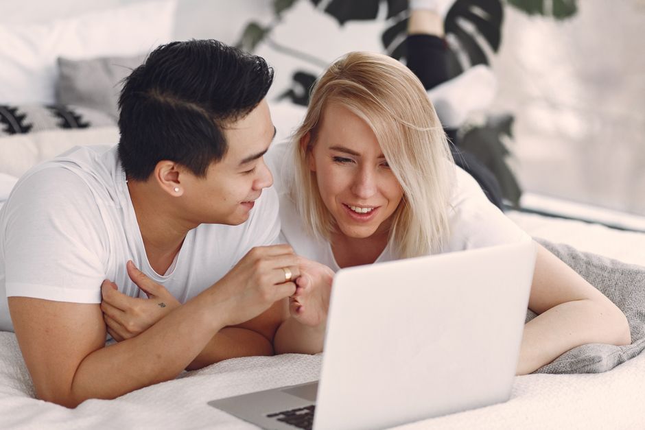 Happy couple enjoying leisure time indoors on laptop, sharing smiles and connection.