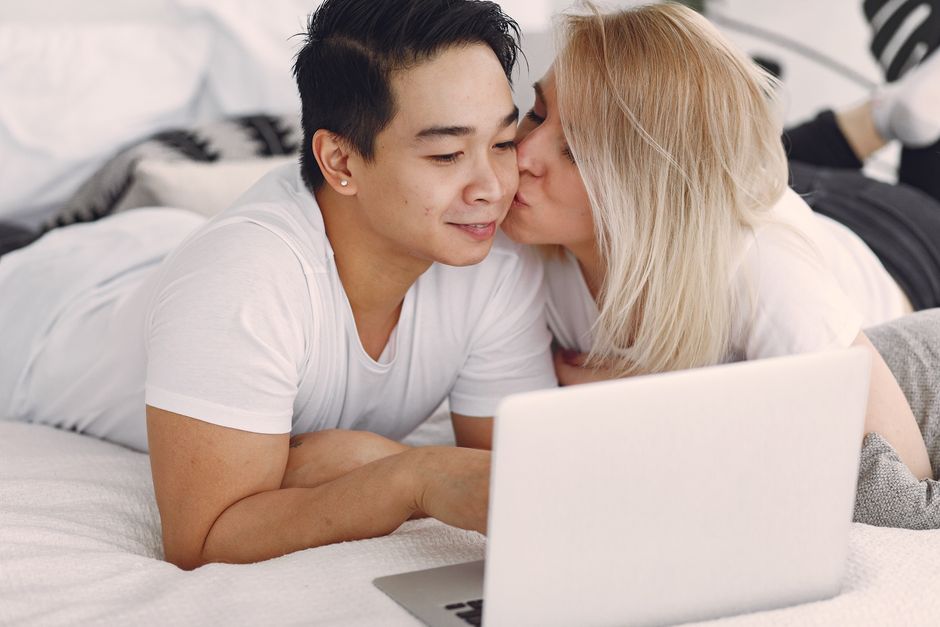 A couple shares a loving moment while browsing on a laptop in their bedroom, highlighting modern relaxation.