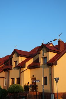 Sunny suburban street with charming houses and distinctive red roofs during sunset.
