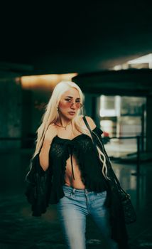 Blonde woman poses confidently indoors wearing a trendy black top and jeans, exuding style and confidence.