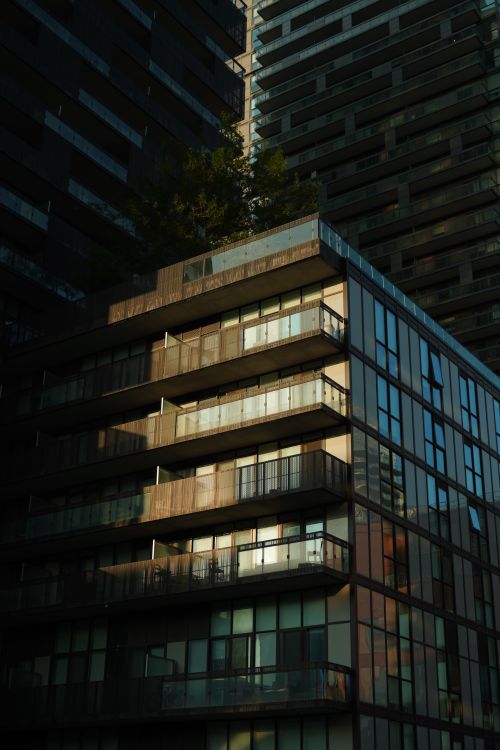 Free A modern apartment building with glass facades illuminated by low sunlight casting shadows. Stock Photo