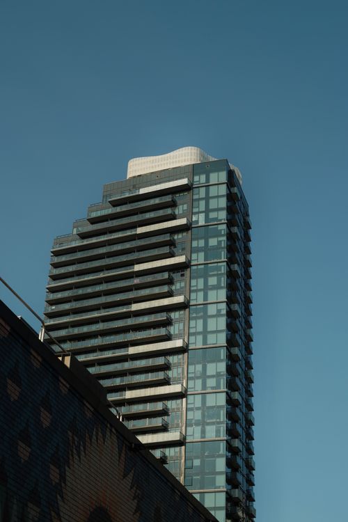 Free A sleek modern skyscraper with glass facade set against a clear blue sky. Stock Photo