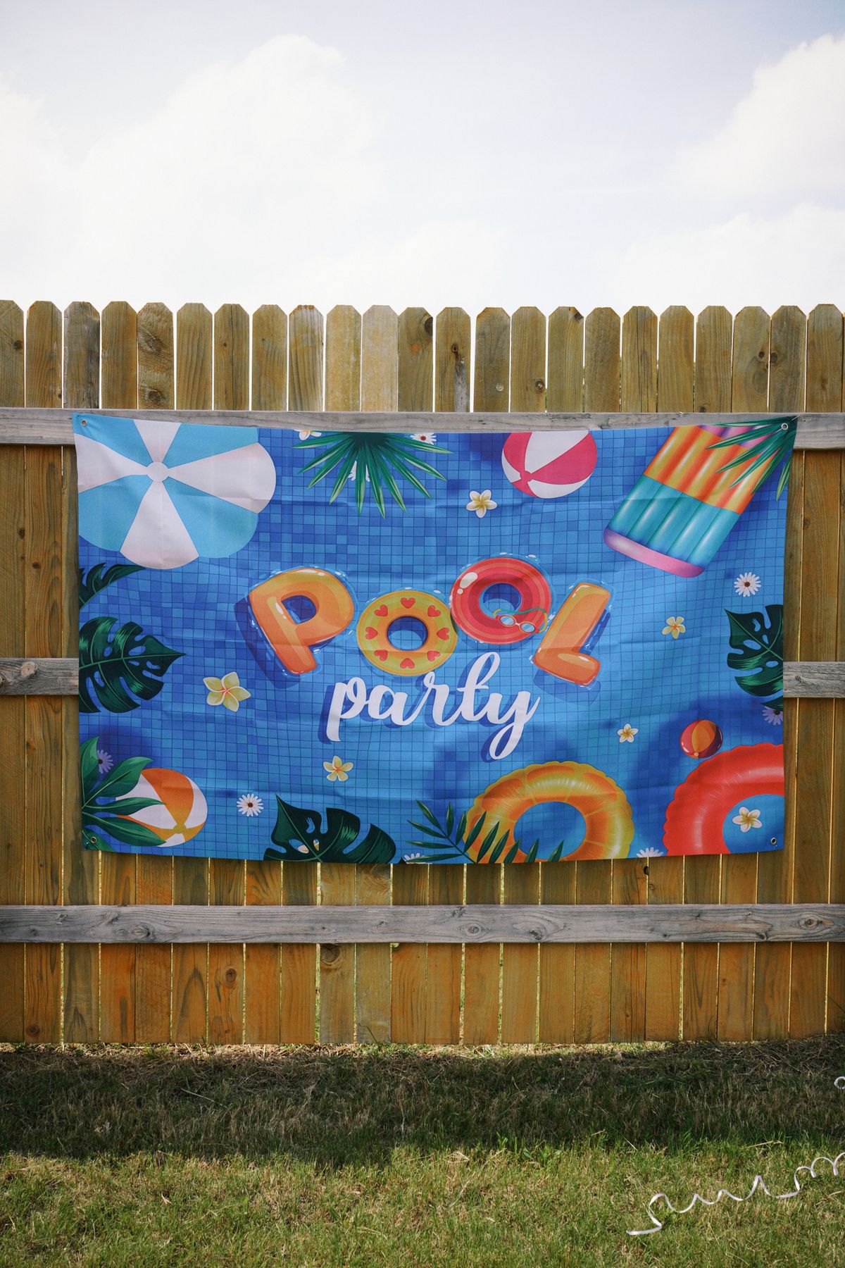 Bright and festive pool party banner with inflatable floats and summer decorations on a wooden fence. Stock Photo.