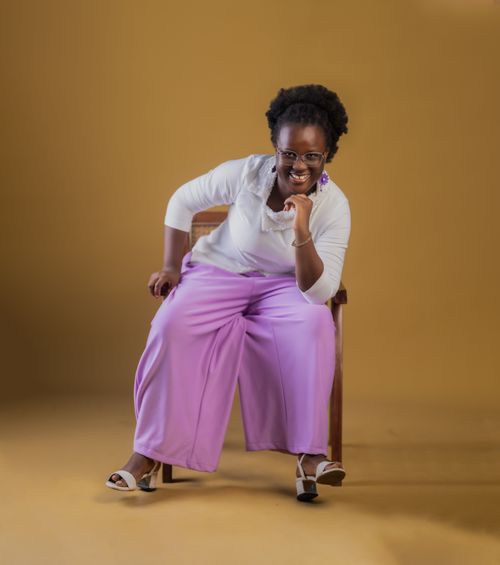 Free A cheerful woman wearing lavender pants sits confidently on a chair, exuding positivity. Stock Photo
