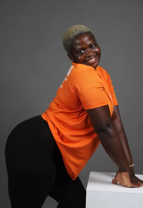 Free Happy person posing with a smile in an orange shirt against a grey background. Stock Photo