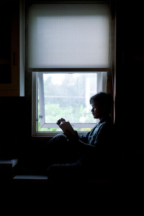 Free Silhouette of a person reading by a window, creating a serene, cozy atmosphere. Stock Photo