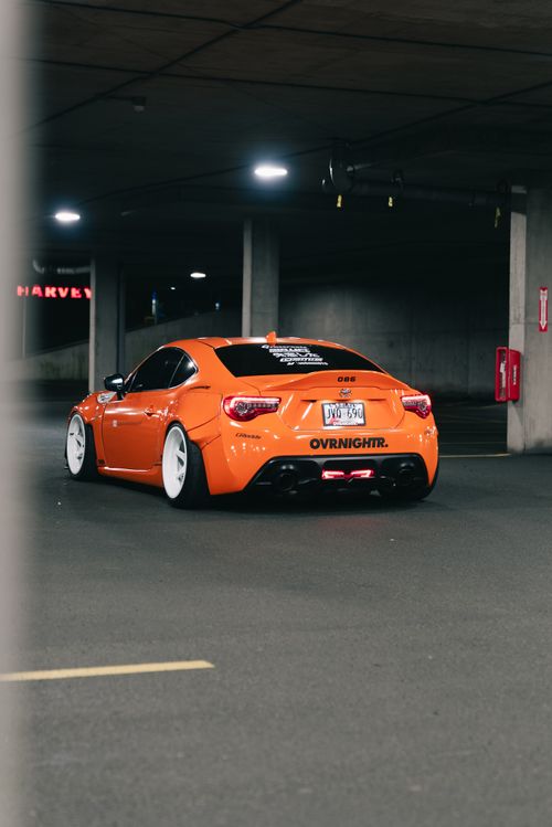 Free Eye-catching orange sports car with white rims in a dimly lit urban parking garage at night. Stock Photo
