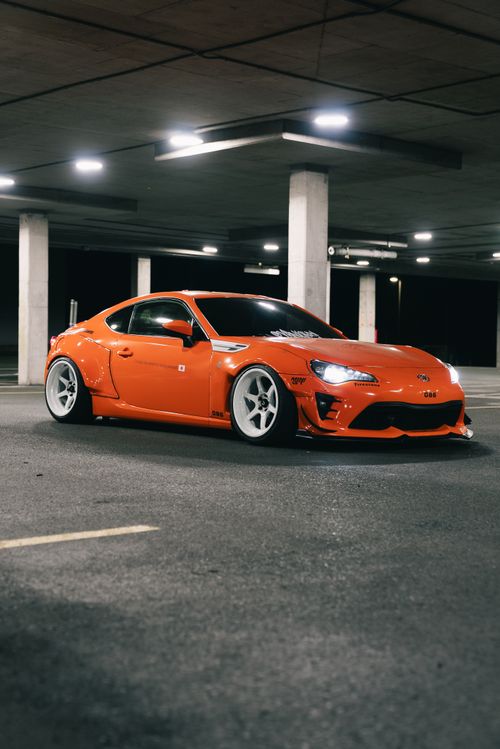 Free Vibrant orange sports car parked in a dimly lit underground garage, showcasing modern automotive design. Stock Photo