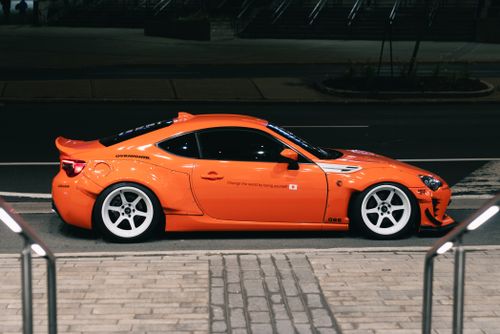Free Sleek orange sports car parked on an urban street at night, showcasing custom wheels and decals. Stock Photo